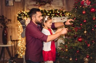 Father and daughter place an ornament on the Christmas tree